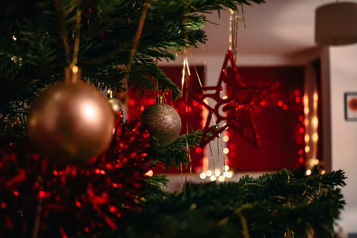 Close-up of Christmas tree ornaments with warm holiday lights in the background.